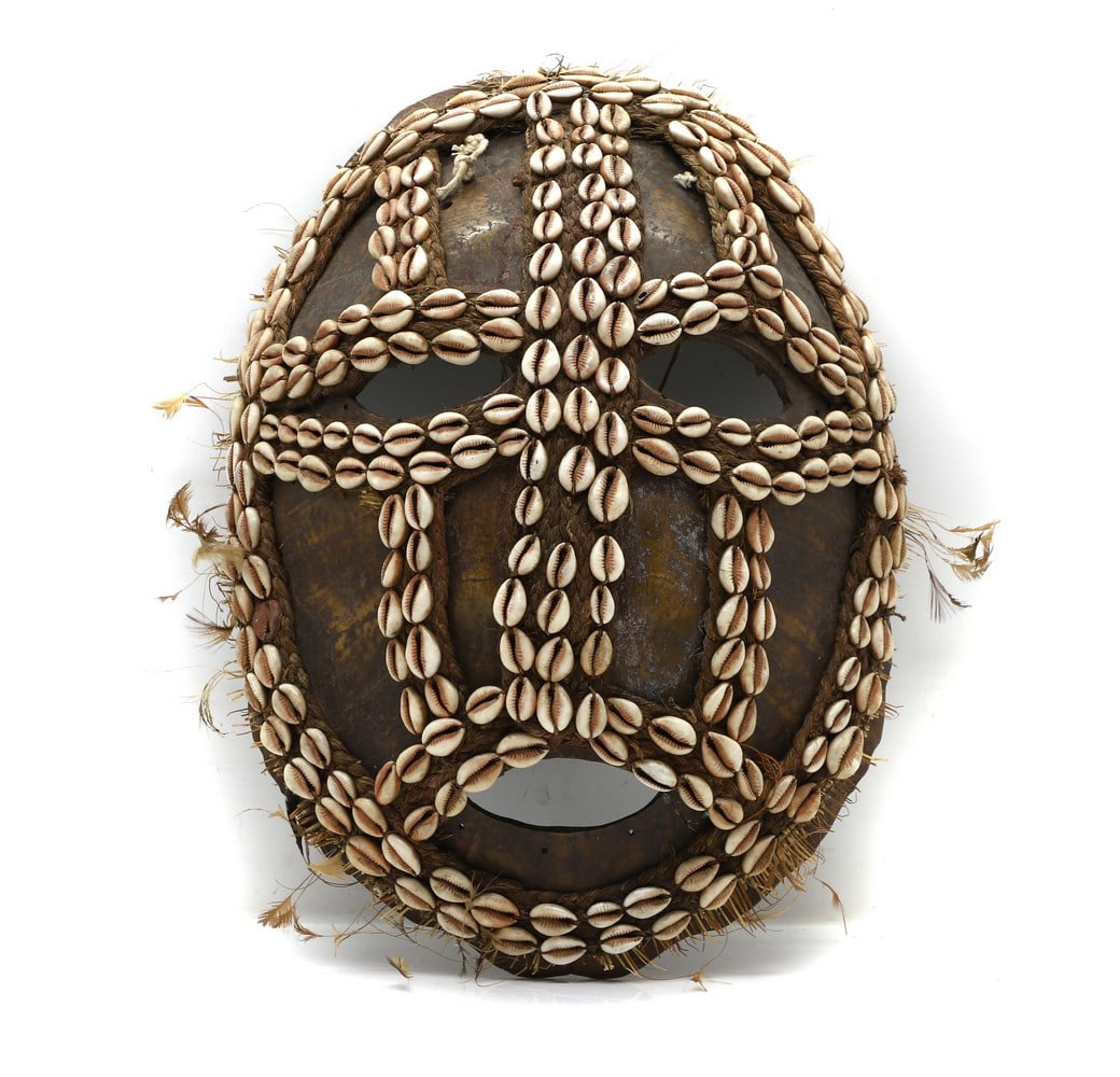 A Papua New Guinea turtle shell mask,: A Papua New Guinea turtle shell mask, 20th century, with applied cowrie shells, feathers, and straw 30cm wide 42.5cm high Condition Report: Minor losses in places.