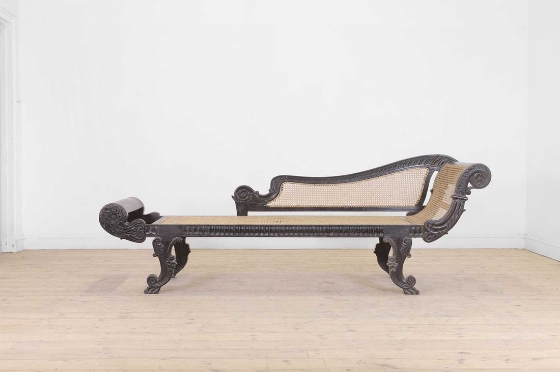 An ebony and cane chaise longue,: An ebony and cane chaise longue, 19th century, Anglo-Indian, on double scroll legs terminating in paw feet, 222cm long 68cm deep 78cm high