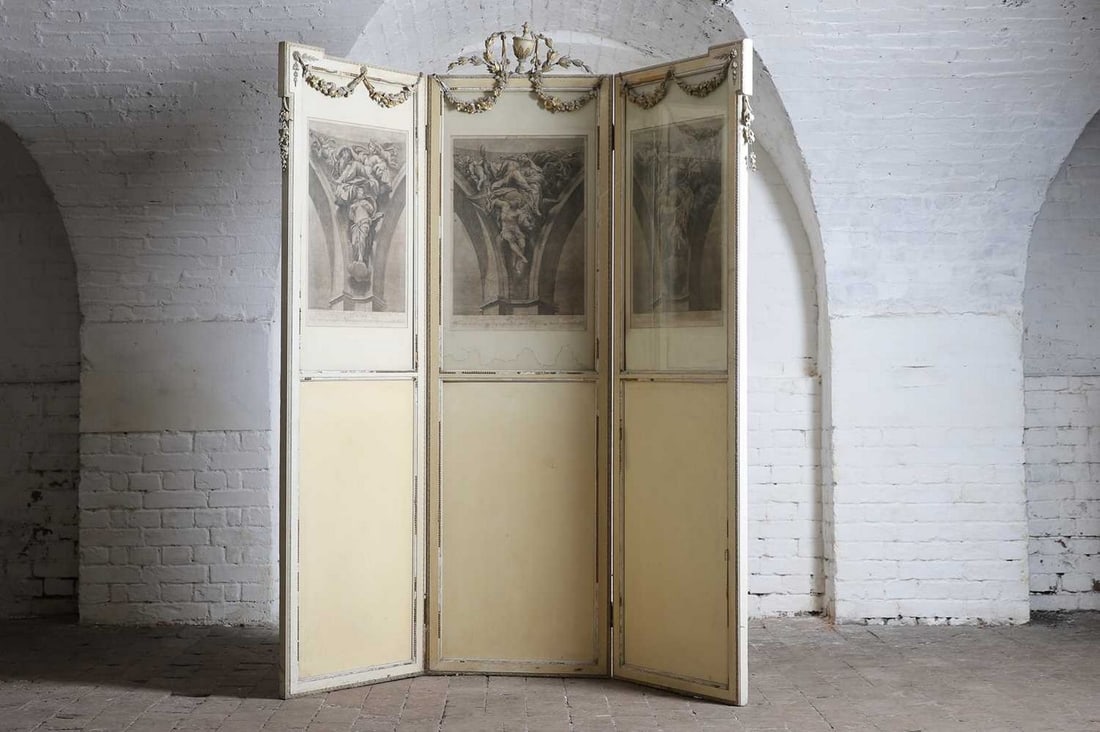 An Edwardian painted three-fold screen,: An Edwardian painted three-fold screen, surmounted by a carved wooden urn and floral swags, with three folds inset with a classical Italian engraving of figural architectural detail, the reverse with