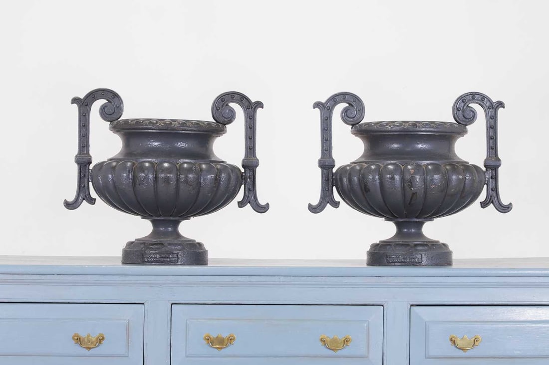 A pair of cast iron garden urns,: A pair of cast iron garden urns, mid-19th century, French, by Alfred Corneau, each with a pair of scrolled handles, enclosing a gadrooned body, cast 'Corneau Alfred A Charleville', 57cm wide 40cm deep