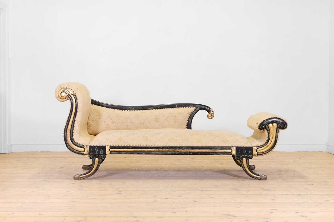 A Regency-style ebonised and parcel-gilt chaise longue,: A Regency-style ebonised and parcel-gilt chaise longue, 20th century, with scrolling foliate detail, raised on outsplayed supports, terminating in brass paw feet, 215cm long 76cm wide 90cm high Condit