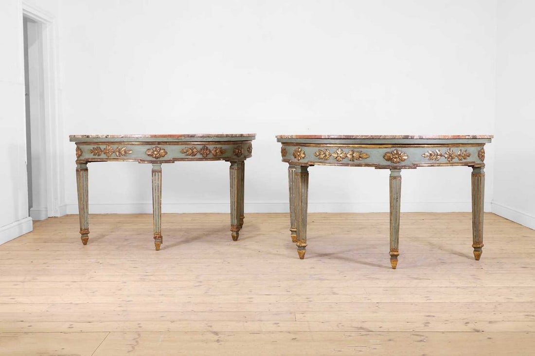 A pair of neoclassical painted and parcel-gilt wooden console tables,: A pair of neoclassical painted and parcel-gilt wooden console tables, 19th century, Italian, each of demilune outline with a marble top and a carved foliate frieze, raised on tapering fluted square su