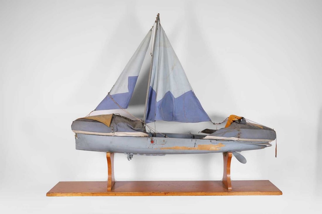A model rescue boat,: A model rescue boat, c.1940s, a prototype of a Second World War Uffa Fox model lifeboat, painted in blue and grey, with stitched cotton sails, painted with wartime signs and markings, raised on a wood