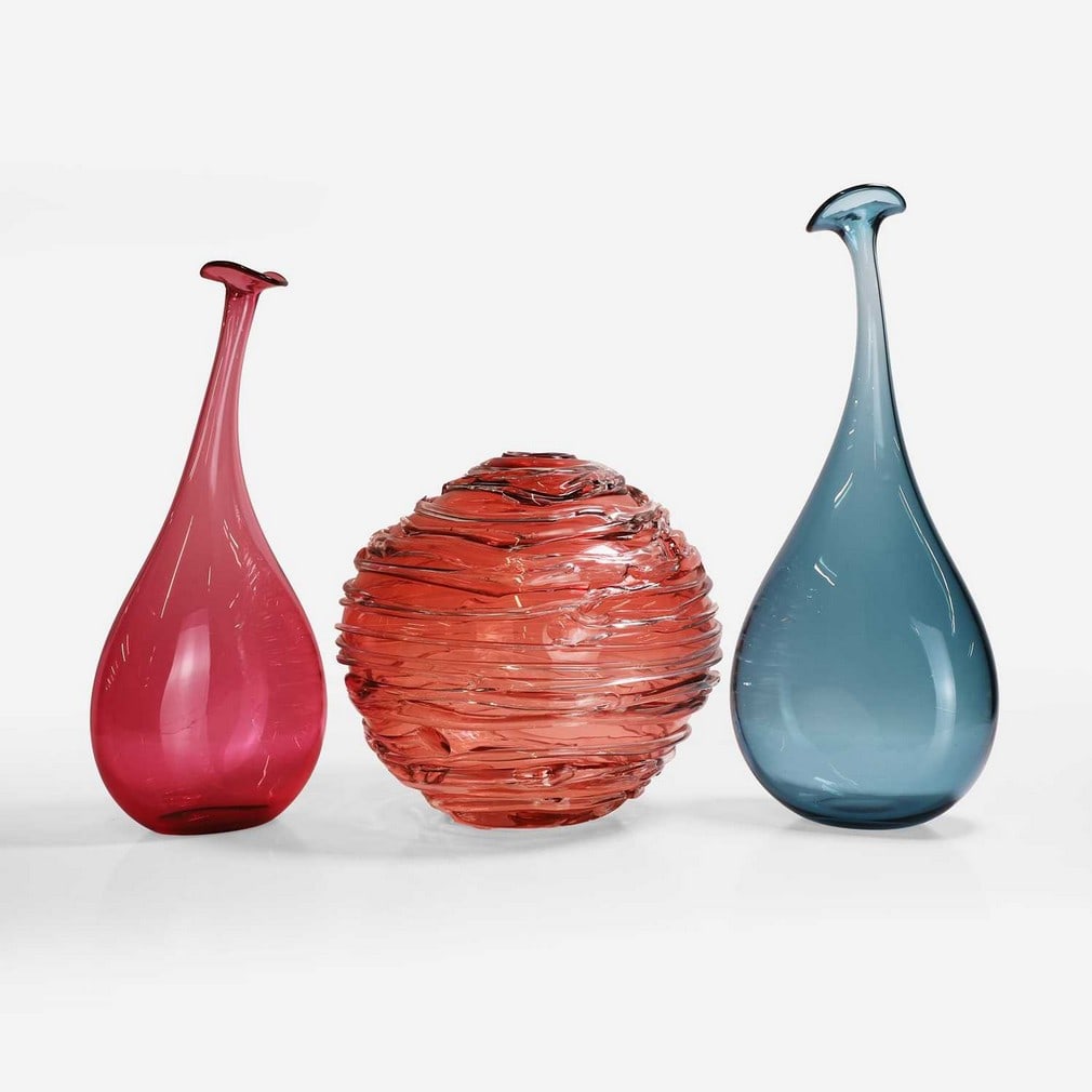 A collection of William Yeoward glass items,: A collection of William Yeoward glass items, comprising: a 'Strata' vase, by Colin Hawkins, with applied clear trails to a pale red ground, engraved signature, 29cm high, and two 'Wonky Bottle' vases,