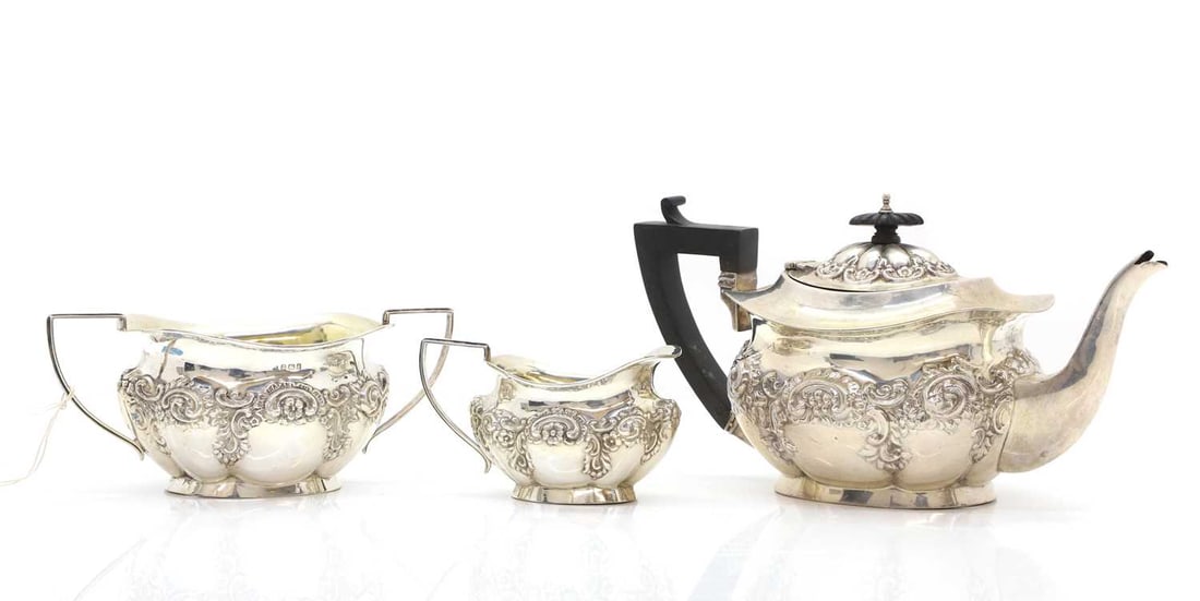 A silver three piece tea service,: A silver three piece tea service, by William Adams Ltd, Birmingham, 1911, comprising a teapot with ebonised handle and finial, 29cm wide, a sugar bowl, 21cm wide, and a cream jug, 13cm wide, all with