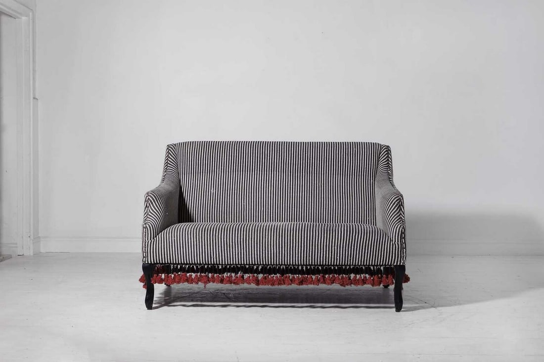 A small upholstered sofa by OKA,: A small upholstered sofa by OKA, of recent manufacture, with studded striped fabric and tasselled detail, raised on black-painted supports, 138cm wide 95cm deep 98cm high Condition Report: Some dirt,