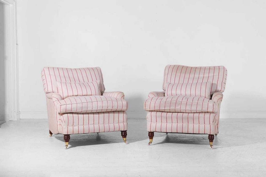 A pair of upholstered armchairs in the Howard & Sons style,: A pair of upholstered armchairs in the Howard & Sons style, of recent manufacture, each with roll arms and feather-filled cushions, raised on turned supports and castors, covered in William Yeoward st