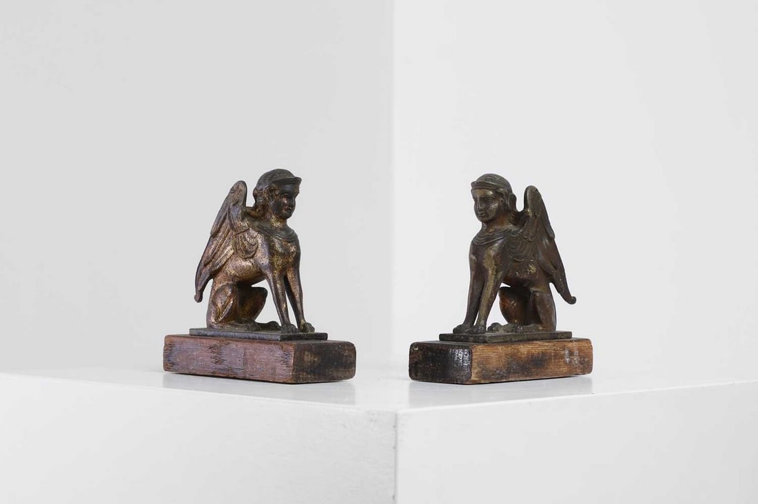 A pair of grand tour gilt-metal bookends,: A pair of grand tour gilt-metal bookends, 19th century, each in the form of a seated sphinx, raised on a wooden plinth, 12.5cm wide 5.5cm deep 13cm high (2) Provenance: An East Anglian Private Collect