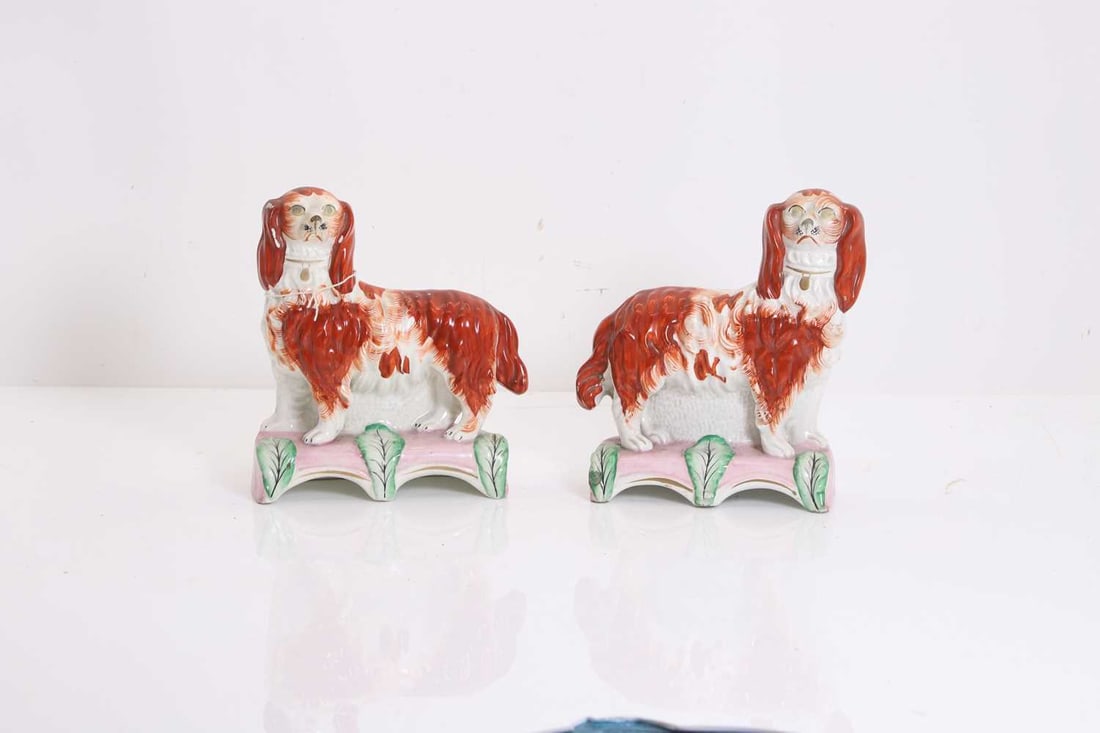 A pair of Staffordshire pottery spaniels,: A pair of Staffordshire pottery spaniels, late 19th/early 20th century, the spaniels both stood on a pink stand, 16cm wide7.2cm deep19.5cm high (2) Condition Report Rubbing to the gilding. Crazing to