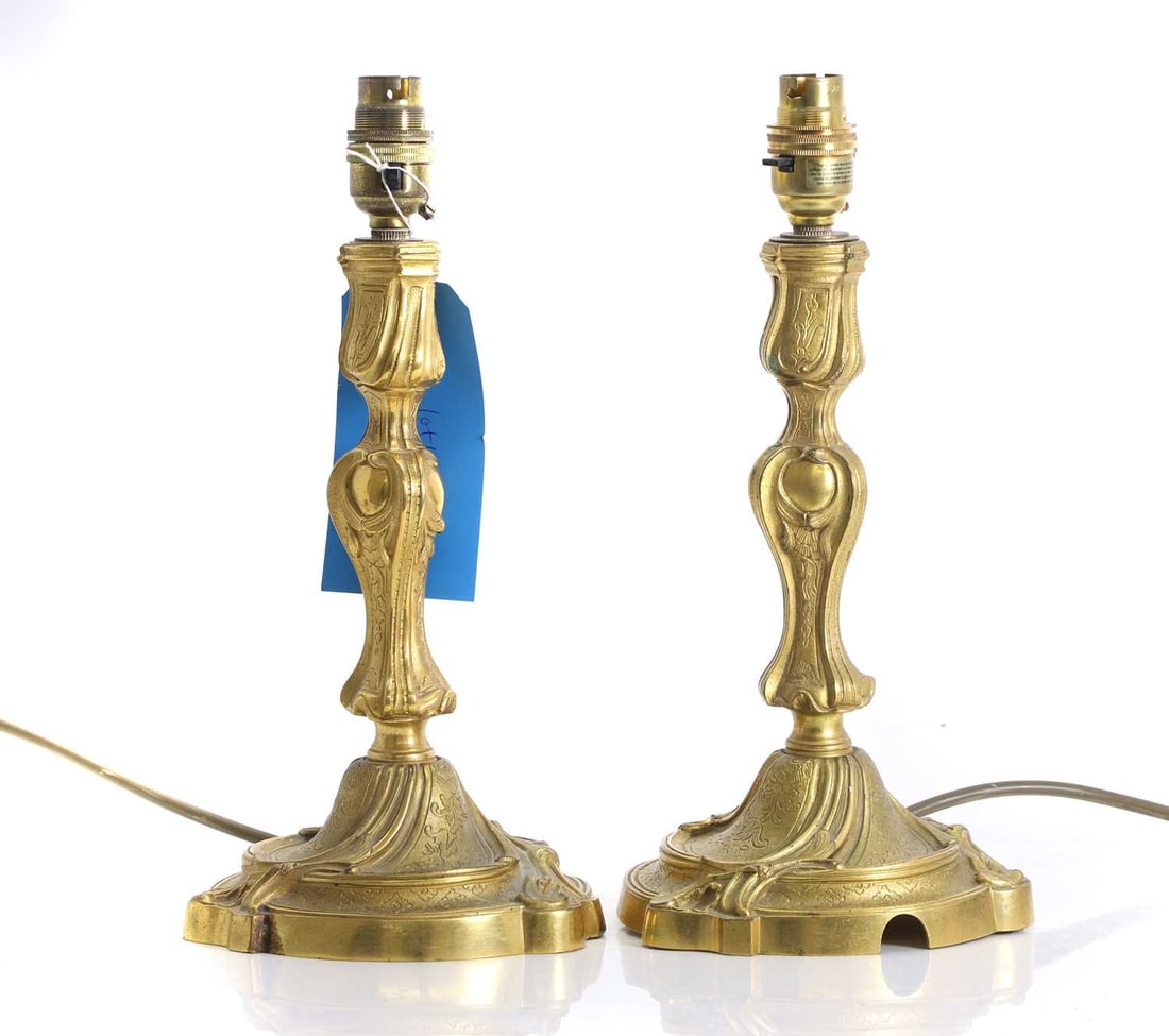 A pair of gilt brass candlestick lamps,: A pair of gilt brass candlestick lamps, 20th century, with scrolled relief decoration to the circular base, and shaped stem, 32cm high (2) Condition Report We cannot g