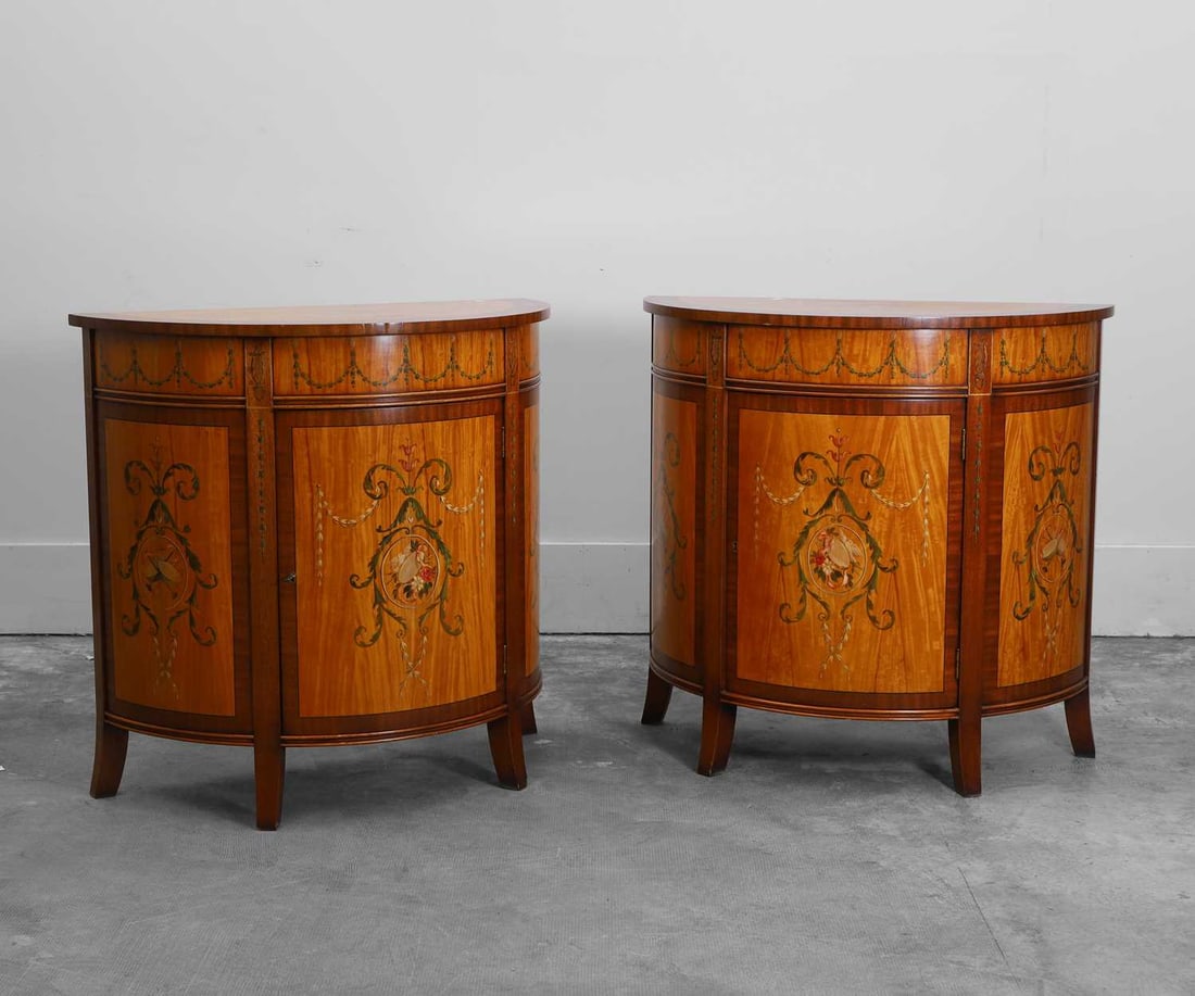A pair of stainwood and mahogany painted demilune cabinets 20th century: A pair of stainwood and mahogany painted demilune cabinets 20th century Of demilune form, painted with musical instruments, husks, swags, and ribbons, the tops with an anthemion border, each enclosin