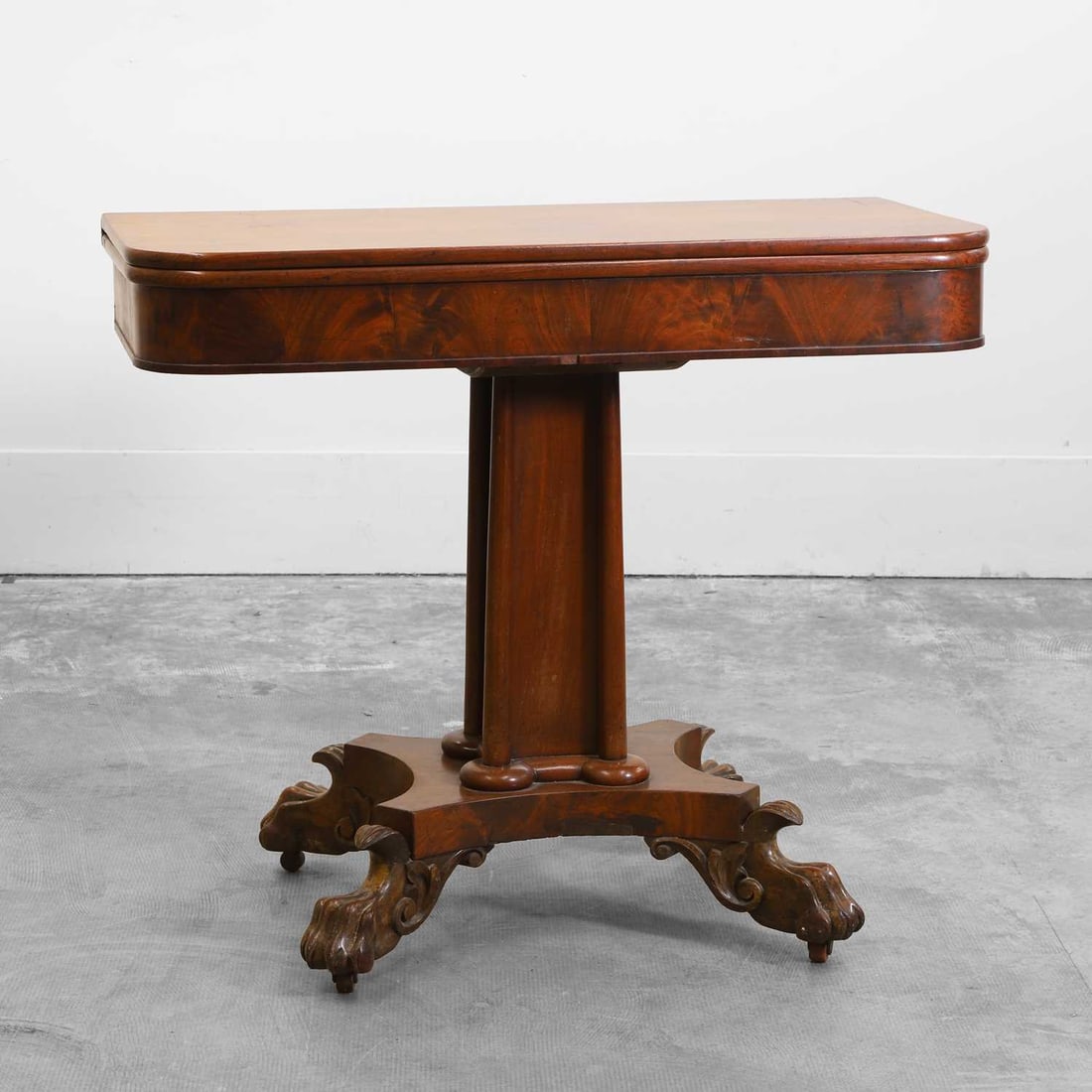An early Victorian mahogany fold over tea table 19th century: An early Victorian mahogany fold over tea table 19th century The rounded rectangular top with a moulded edge, above a plain frieze raised on a pedestal and quadriform base with carved claw feet and c