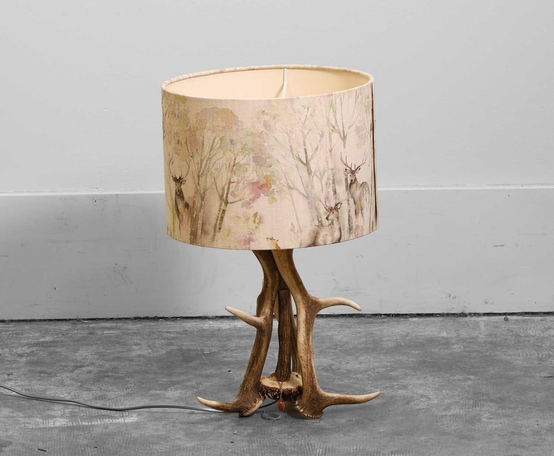 An antler table lamp with stag-print shade, Of recent manufacture: An antler table lamp with stag-print shade, Of recent manufacture Natural intertwined antlers supporting fabric shade hand-painted with woodland stag imagery 48.5cm high Shade diameter 31cmCondition