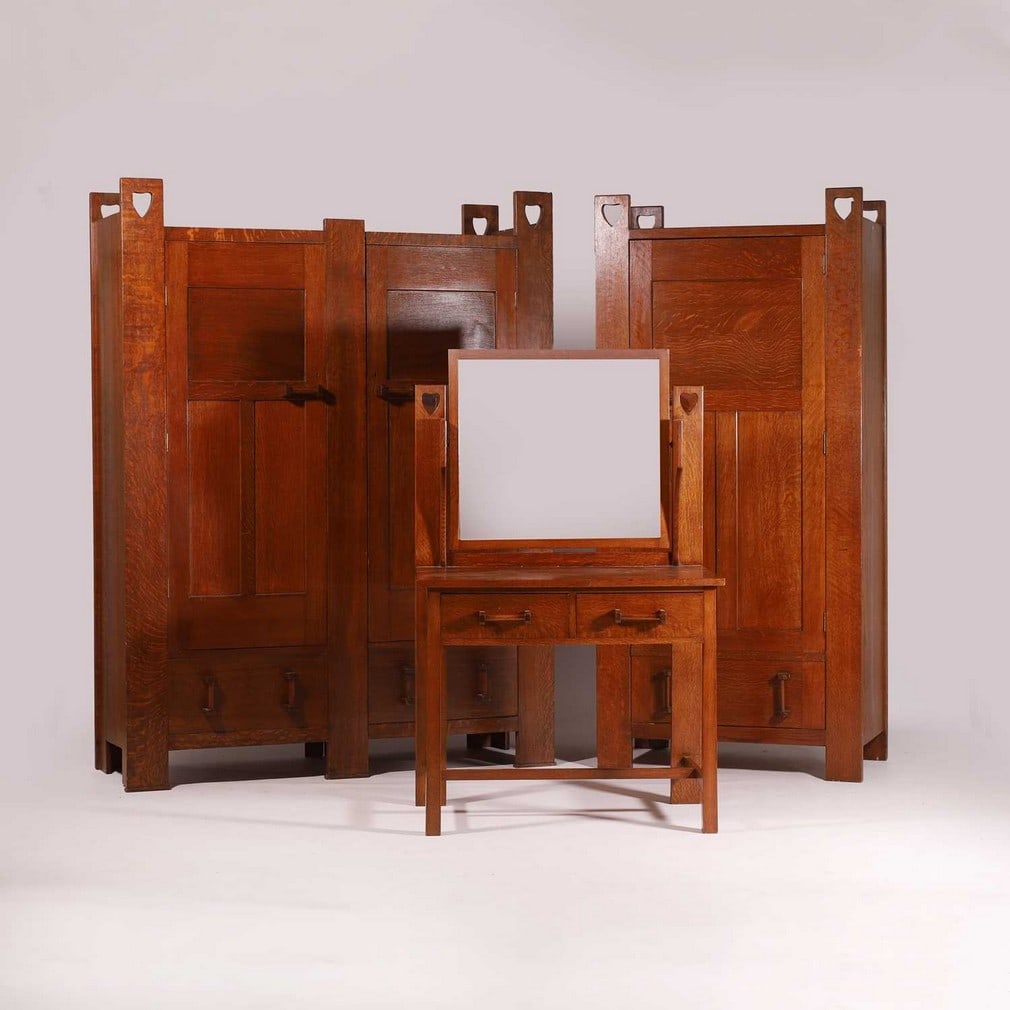 Liberty & Co. An 'Athelstan' dressing table and two wardrobes: Liberty & Co. An 'Athelstan' dressing table and two wardrobes Oak, c.1905, designed by Leonard Wyburd, each piece with fret-cut heart-shaped details, stamped to the brass, comprising: a dressing table