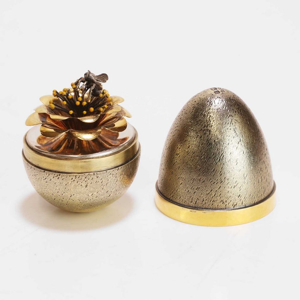 ▲ Stuart Devlin (Australian-British, 1931-2018) A silver and silver-gilt surprise egg: ▲ Stuart Devlin (Australian-British, 1931-2018) A silver and silver-gilt surprise egg London 1981, the textured silver-gilt exterior opening to reveal a bee perched on a flower, with yellow enam