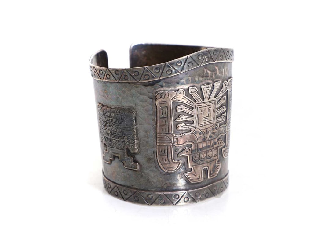 A Peruvian silver cuff bracelet, 20th century: A Peruvian silver cuff bracelet, 20th century With applied motifs of three figures, and banded by an angular repetitive triangle and dot section, 6cm diameter 6.5cm high 2.6ozt