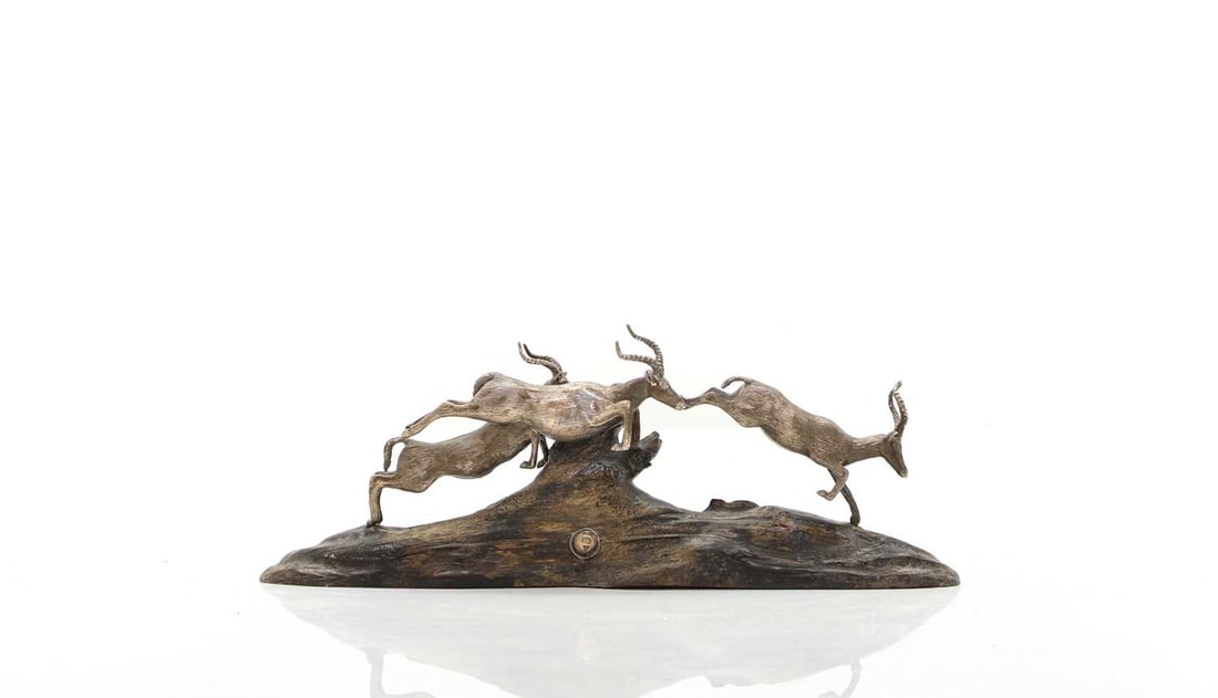 A silver and wood model of leaping impalas By Patrick Mavros, Zimbabwe, 20th century: A silver and wood model of leaping impalas By Patrick Mavros, Zimbabwe, 20th century Depicting the three jumping over a mound in unison, signed 'PM' on a lower mounted silver roundel, 21cm long