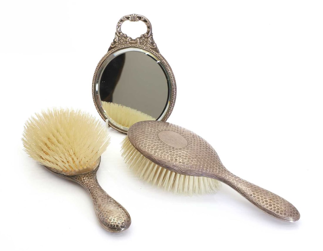 A matched silver-backed dressing mirror and a pair of brushes,: A matched silver-backed dressing mirror and a pair of brushes, Birmingham and Chester, various dates, each with hammered backs 17.5cm and 24.5cm long3Condition Report: Tarnished. Chester and Birmingh