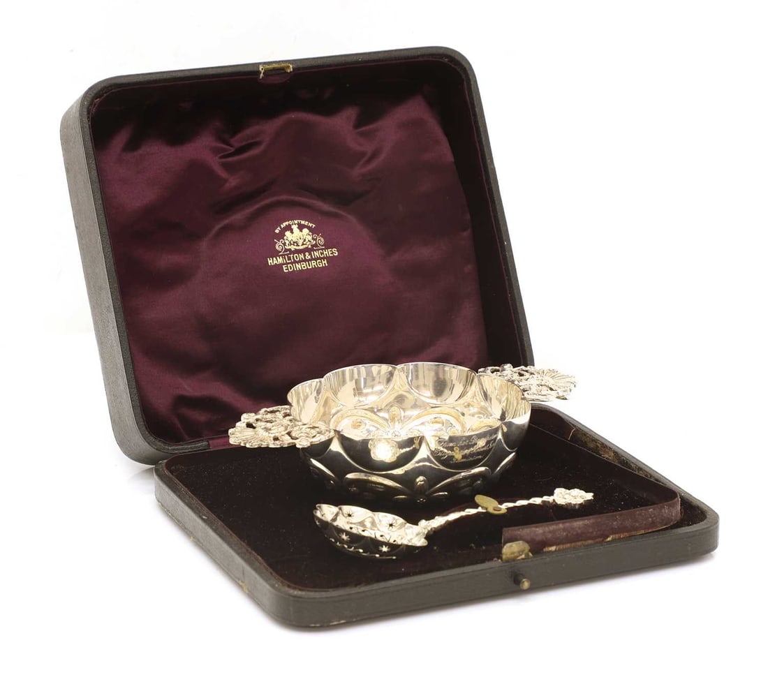 A silver twin handled sugar bowl, and spoon,: A silver twin handled sugar bowl, and spoon, By Hamilton and Inches, Edinburgh, 1904, with an engraved inscription, cased 17.7cm wide, spoon, 13cm long, 4.9ozt Condition Report: Fair overall. Case