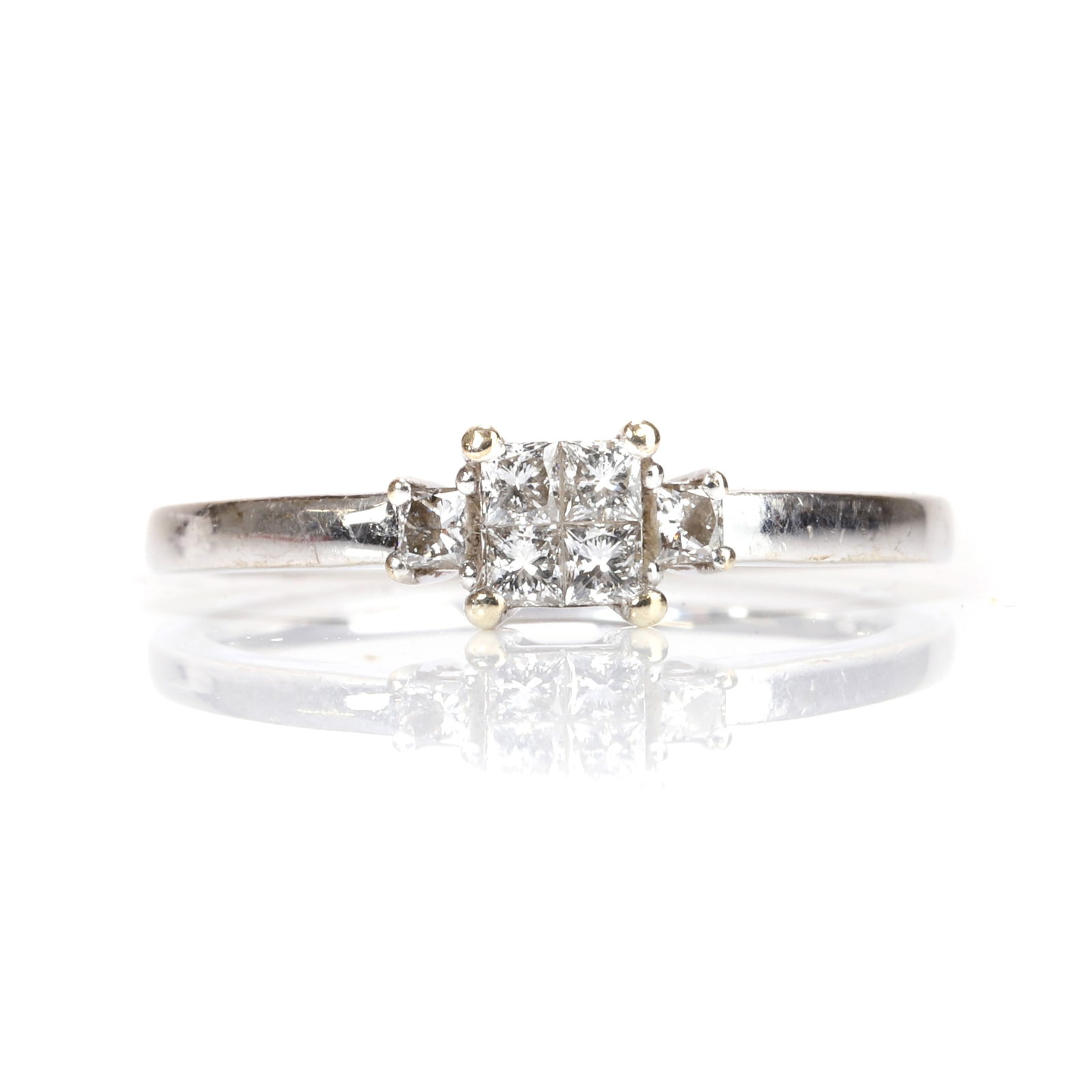 A 9ct white gold diamond ring,: A 9ct white gold diamond ring, claw set to the centre with a cluster of four princess cut diamonds, flanked by a princess cut diamond to either side, into a squared profile shank, hallmarked Edinburgh