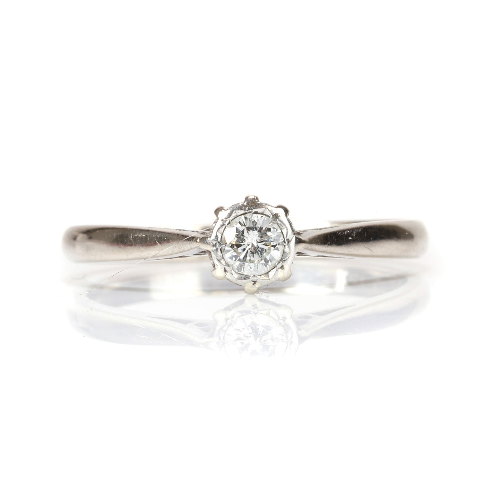 An 18ct white gold diamond single stone ring,: An 18ct white gold diamond single stone ring, the illusion collet set with a round brilliant cut diamond, to tapered chenier shoulders and a 'D' profile shank, Birmingham 1977 (Ring size O; 2.6g) Foot