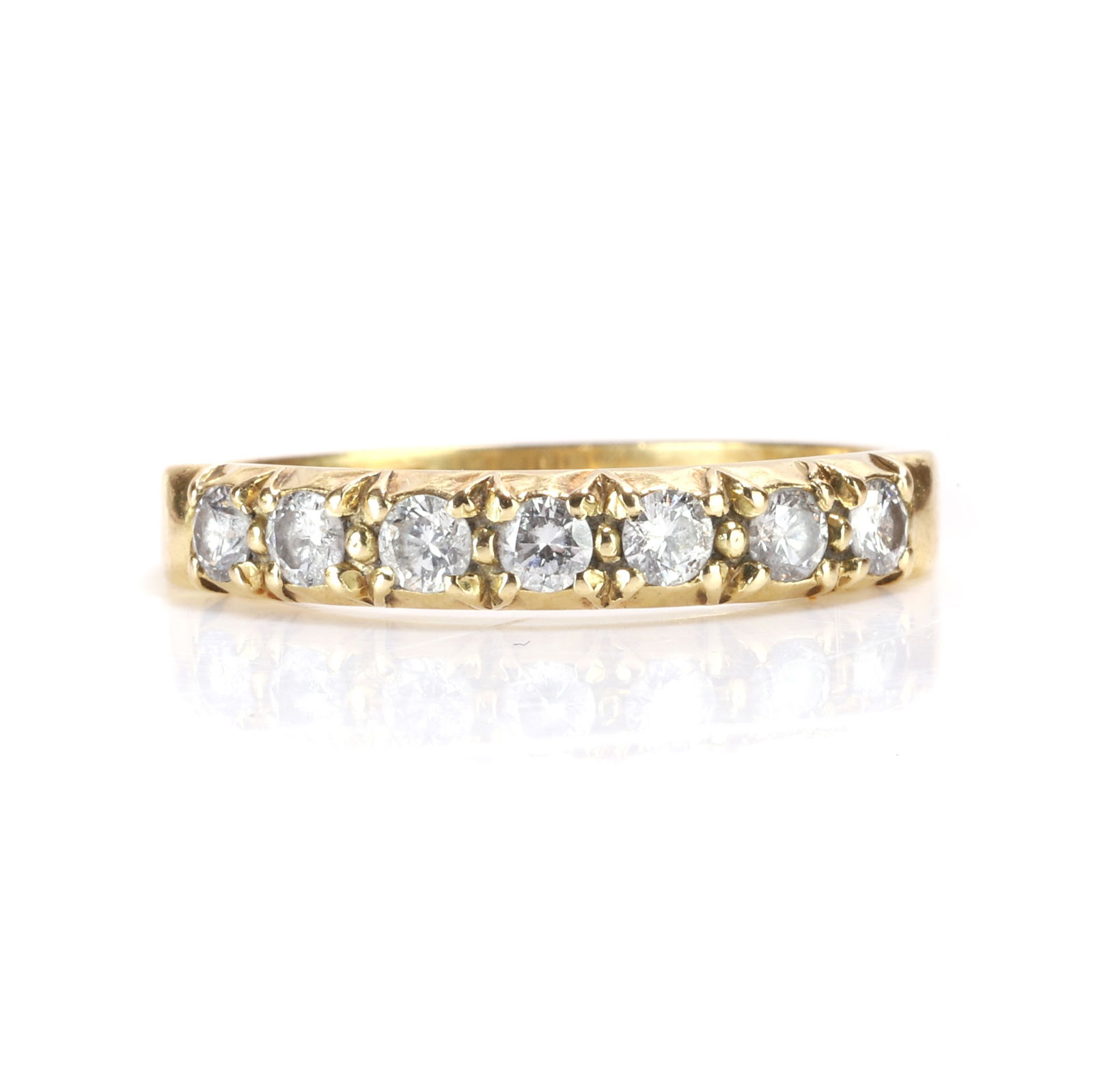 An 18ct gold diamond half eternity ring,: An 18ct gold diamond half eternity ring, claw set with a line of seven round brilliant cut diamonds, into tapered shoulders and a 'D' profile shank, London 1994 (Ring size M; 2.6g) Footnote: Buying