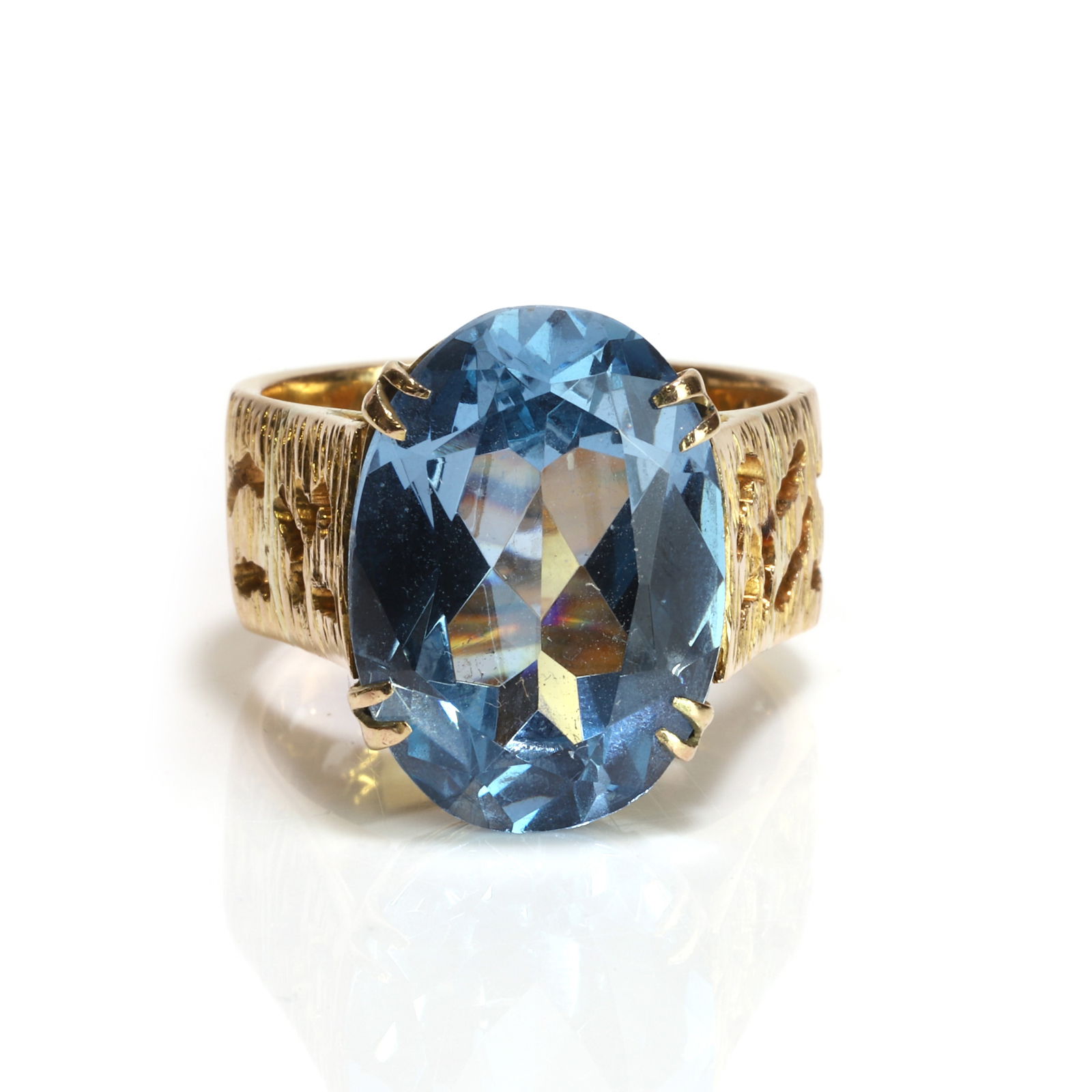 An 18ct gold synthetic blue spinel ring,: An 18ct gold synthetic blue spinel ring, claw set with an oval cut synthetic blue spinel to a pierced under bezel, into a pierced and textured flat profile shank, hallmarked Birmingham (Ring size