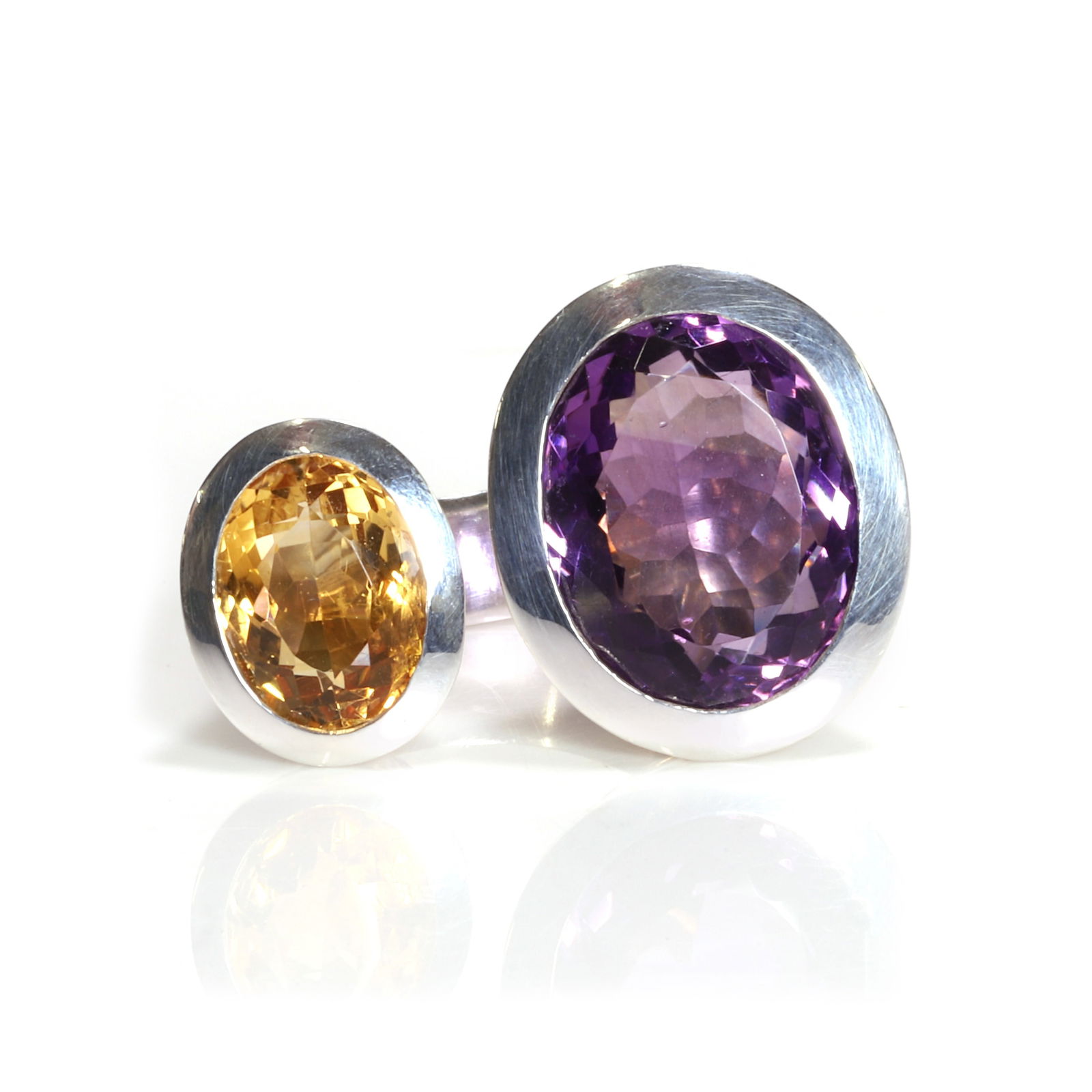 An amethyst and citrine ring,: An amethyst and citrine ring, bezel set with an oval cut amethyst and an oval cut citrine, to an open shank with a 'D' profile, tested as silver (Ring size O; 17.6g) Footnote: Buying this gemston
