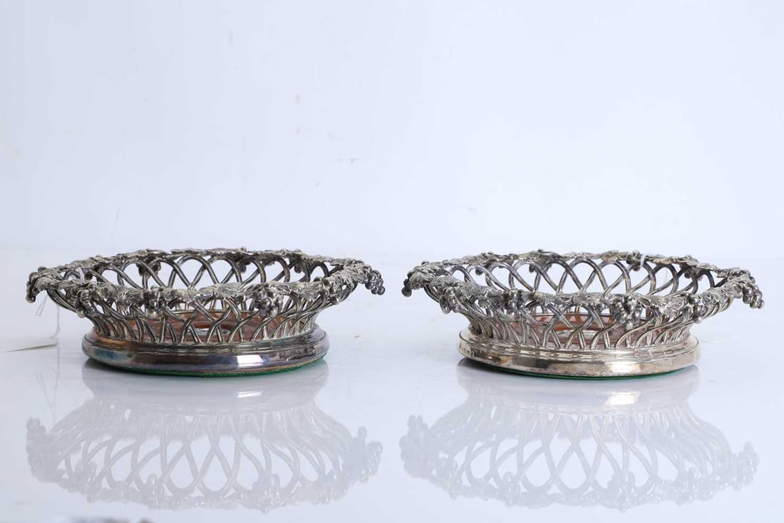 A pair of silver-plated wine coasters, Mid 19th century,: A pair of silver-plated wine coasters, Mid 19th century, by Elkington & Co, of circular form with pierced and interlaced sides cast as trailing vine leaves and grape clusters, the rim richly mode