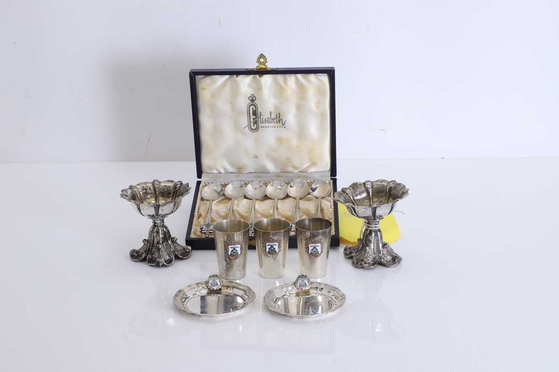 A collection of Hondurous silver and enamelled souvenir spoons,: A collection of Hondurous silver and enamelled souvenir spoons, the tops with an enamelled coat of arms, and three silver shot glasses with a similar enamelled badge to the exterior, together with