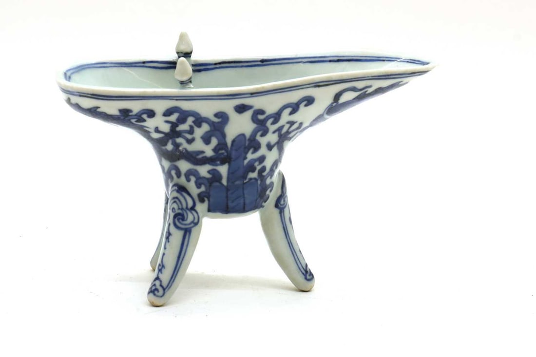 A Chinese blue and white jue cup, 20th century: A Chinese blue and white jue cup, 20th century raised on three slightly curved legs, with one looped handle to the side and two posts with whorl bosses rising from the rim, painted with a dragon