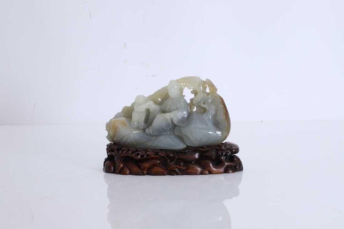 A carved jade figural group, 20th century, Chinese,: A carved jade figural group, 20th century, Chinese, of Guanyin holding a string of beads with a boy, on a rocky landscape with a pine tree above, positioned on a hardwood base carved with pine