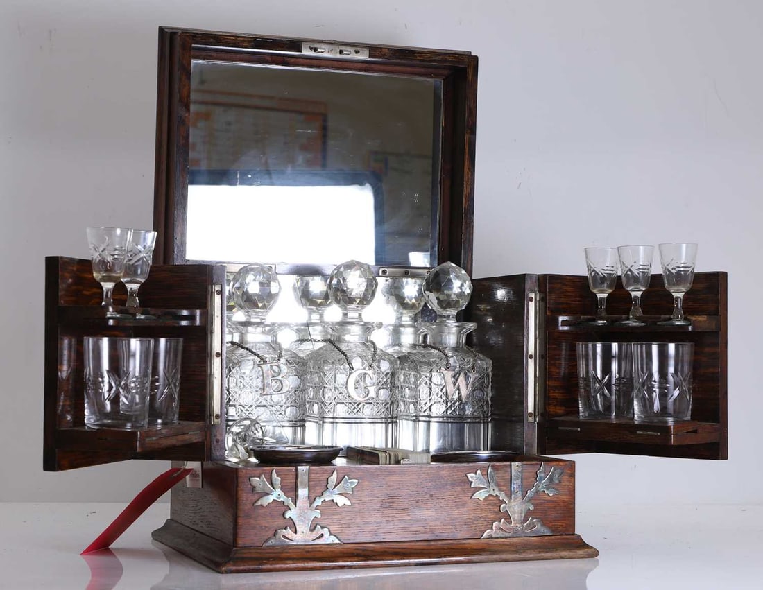 A late Victorian oak travelling tantalus with cut glass decanters and glasses, Late 19th century,: A late Victorian oak travelling tantalus with cut glass decanters and glasses, Late 19th century, the hinged rectangular case with metal mounted corners and escutcheon, the rising lid inset with a mi