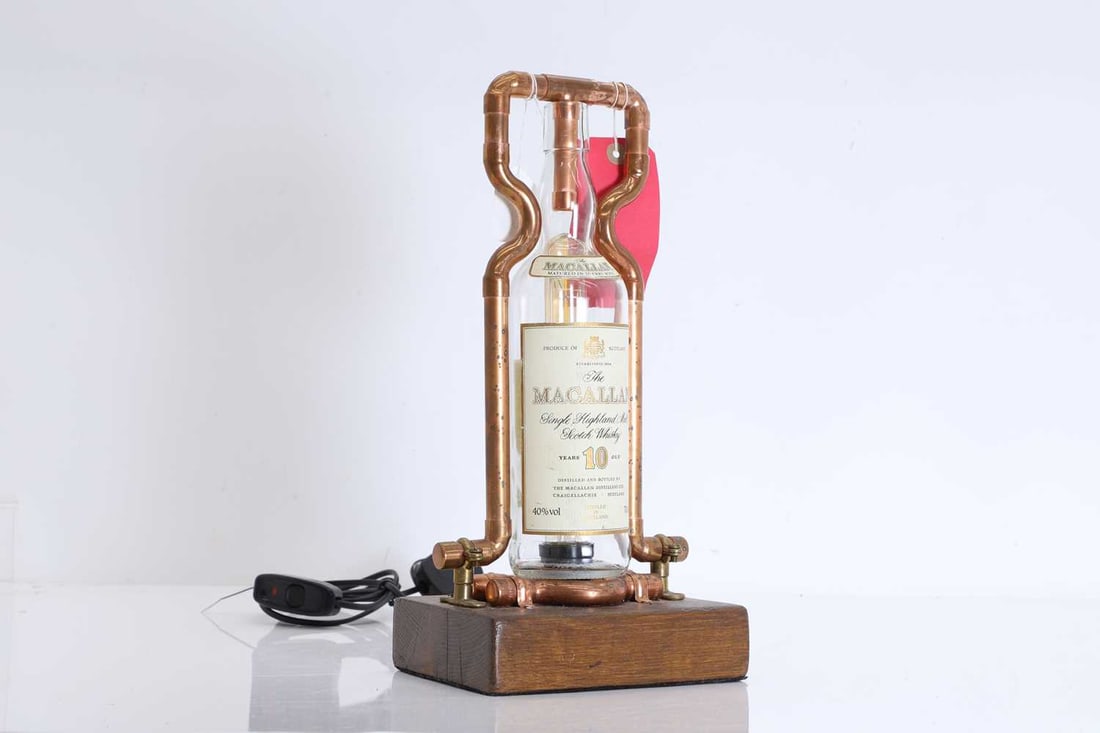 A contemporary table lamp, Of recent manufacture,: A contemporary table lamp, Of recent manufacture, using a Macallan 10 year old whiskey bottle, mounted on a wooden base and secured with copper piping 18cm wide, 39cm high