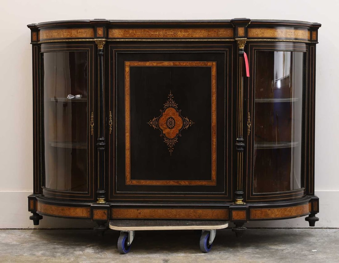 A Victorian ebonised, walnut, and gilt-metal credenza, Late 19th century: A Victorian ebonised, walnut, and gilt-metal credenza, Late 19th century of curved outline, the moulded top above a central panel door inlaid with a scrolling foliate and rosette motif within a gilt-