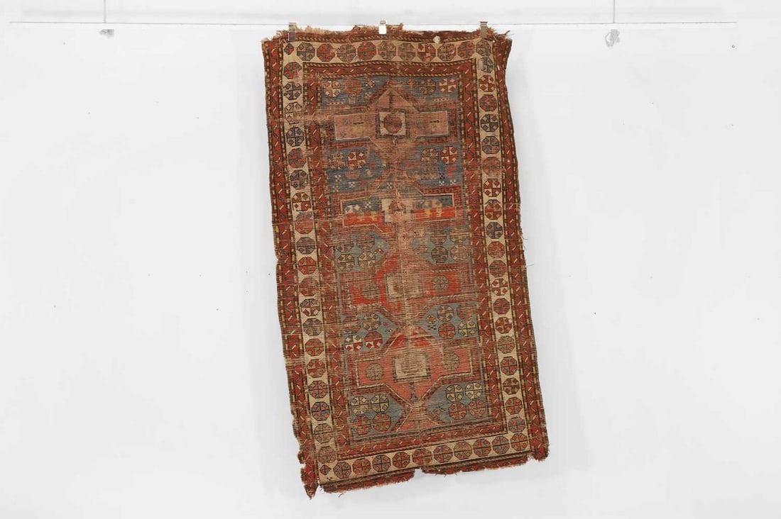 A tribal wool rug, early 20th century, Caucasian,: A tribal wool rug, early 20th century, Caucasian, woven with repeating geometric motifs to a red ground, distressed (215 x 123cm) Provenance: The Richard Collins Collection. Condition Report: Heavily