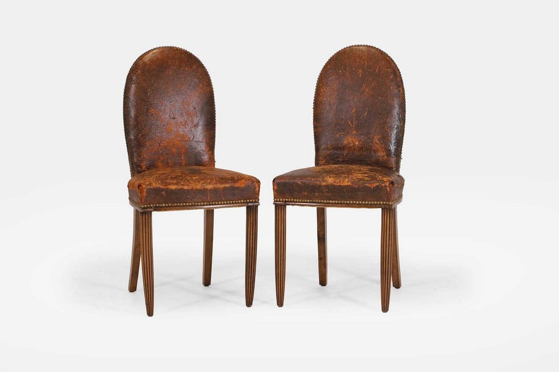 A pair of studded leather and beech side chairs, 20th century,: A pair of studded leather and beech side chairs, 20th century, each with an arched back and a rounded seat, raised on tapering lobed front supports (46cm wide, 48cm deep, 96cm high) (2) Provenance: Th