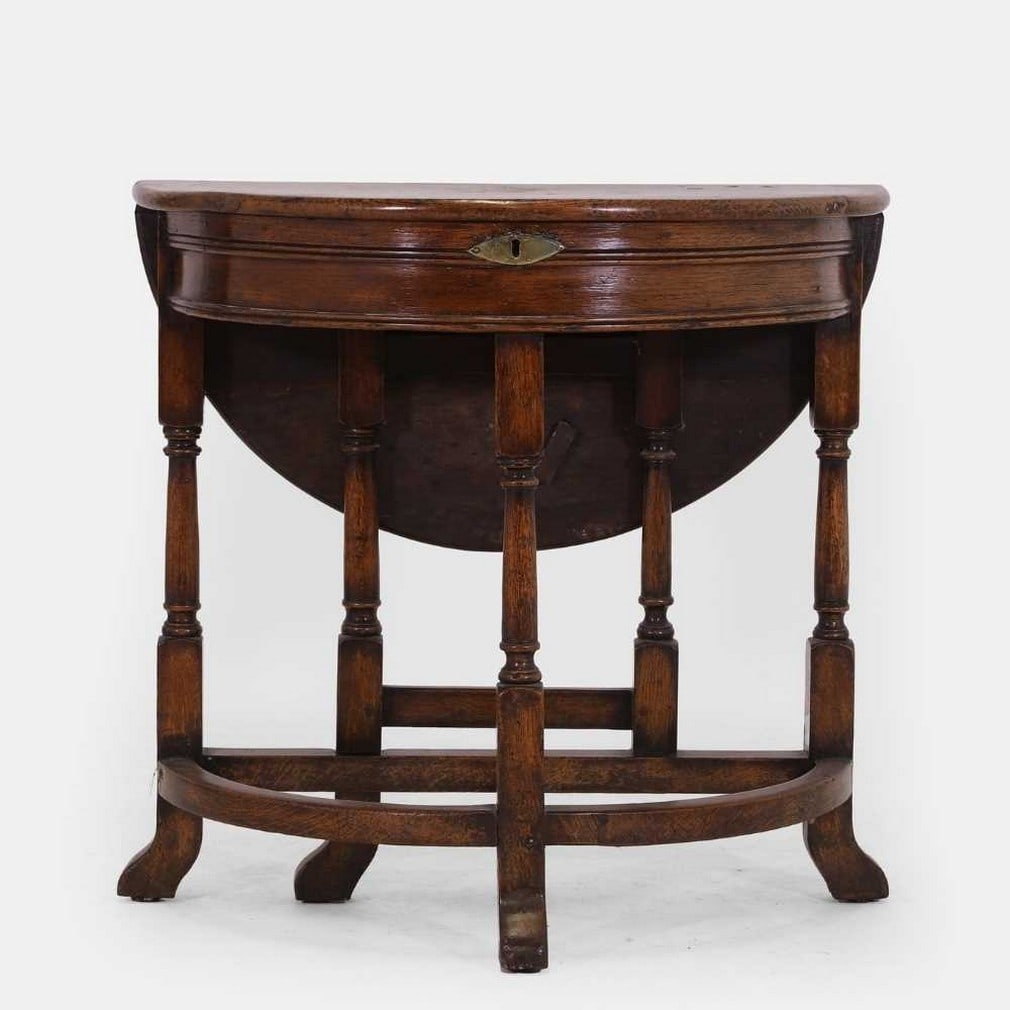 A William and Mary oak credence table, late 17th century,: A William and Mary oak credence table, late 17th century, of demilune outline with a folding top enclosing a well, with a gateleg action, raised on ring-turned supports united by stretchers, terminati