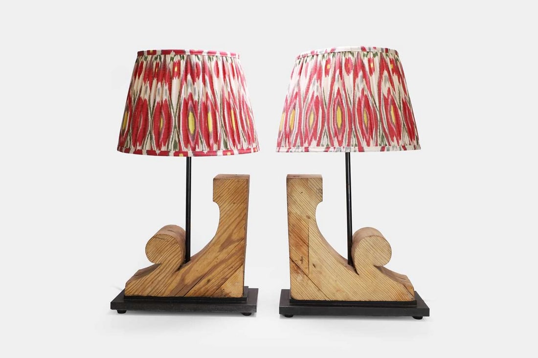 A pair of carved corbel table lamps, 20th century, comprising earlier elements,: A pair of carved corbel table lamps, 20th century, comprising earlier elements, each raised on a black-painted rectangular base and fitted with a 14-inch ikat-printed shade (36cm wide, 15cm deep, 64cm