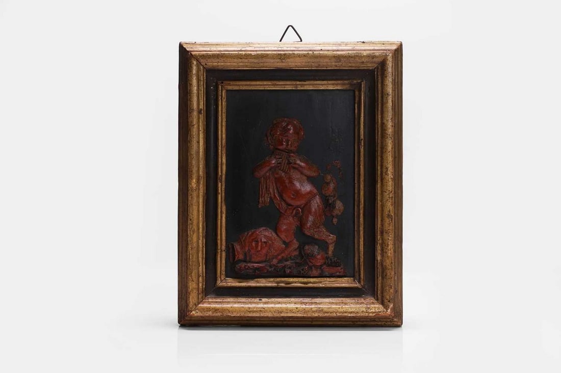 A red wax relief of a young faun playing the pipes, first quarter of the 18th century, Italian,: A red wax relief of a young faun playing the pipes, first quarter of the 18th century, Italian, mounted on a rectangular slate ground, in a moulded, painted and giltwood frame (frame 28 x 22cm) Condit