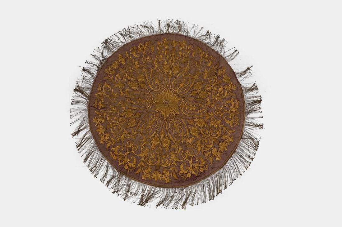 An Ottoman gilt-metal thread and velvet embroidered panel, 19th century, Turkish,: An Ottoman gilt-metal thread and velvet embroidered panel, 19th century, Turkish, of circular form with a tasselled fringe terminating in spangles, the plum velvet ground densely decorated in gold thr