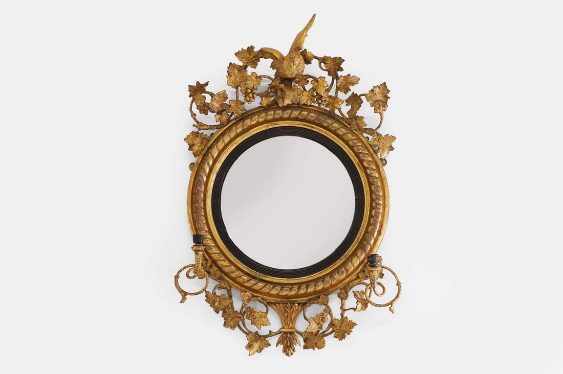A Regency giltwood and gesso convex mirror, c.1815,: A Regency giltwood and gesso convex mirror, c.1815, surmounted by a ho-o bird within fruiting vines, with a moulded frame and a reeded painted slip, issuing a pair of scrolling branches (73cm wide, 21
