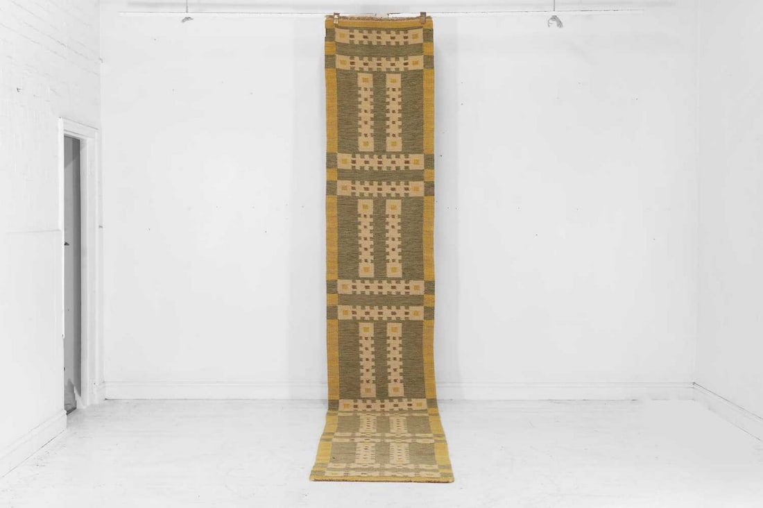 A flat-weave wool runner of Scandinavian design, of recent manufacture, in the manner of Barbro: A flat-weave wool runner of Scandinavian design, of recent manufacture, in the manner of Barbro Nilsson, woven with geometric motifs in tones of green and yellow (454 x 74cm) Condition Report: Very go