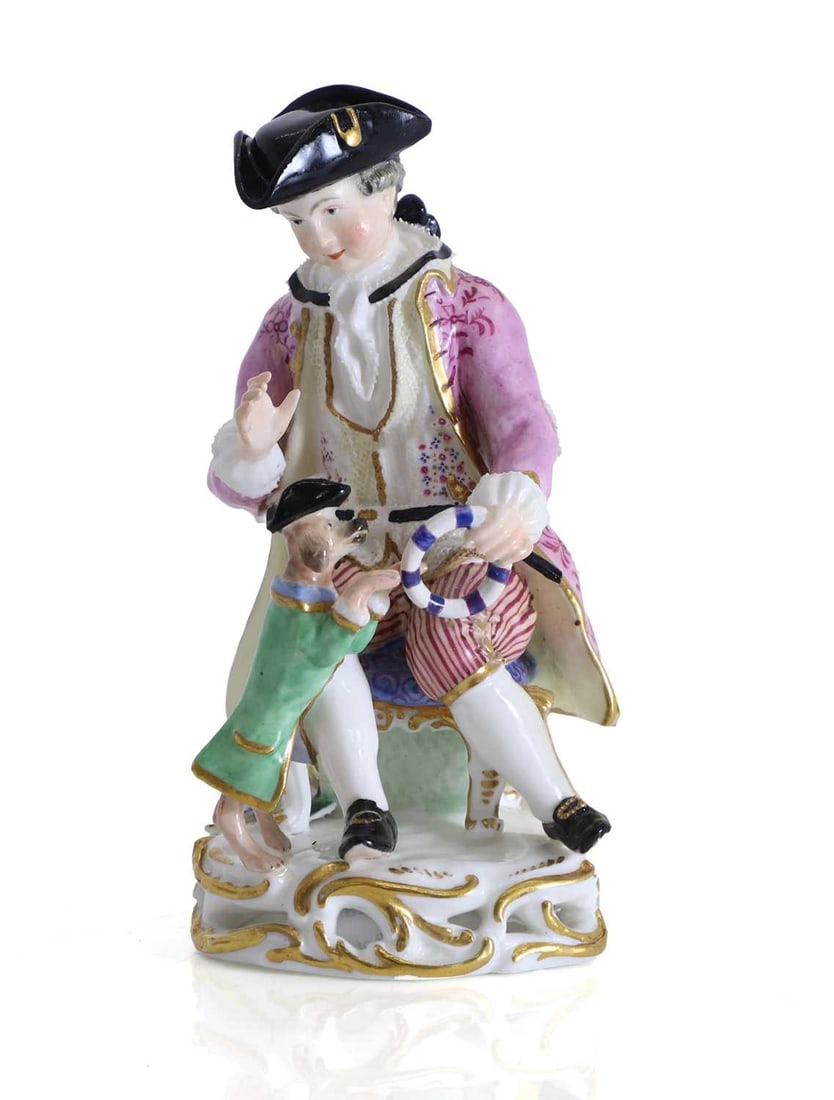 A Continental group as a seated gentleman and his performing dog, late 19th century,: A Continental group as a seated gentleman and his performing dog, late 19th century, modelled gentleman seated upon a rocaille base with gilt scrollwork, wearing a black tricorn hat, puce coat,