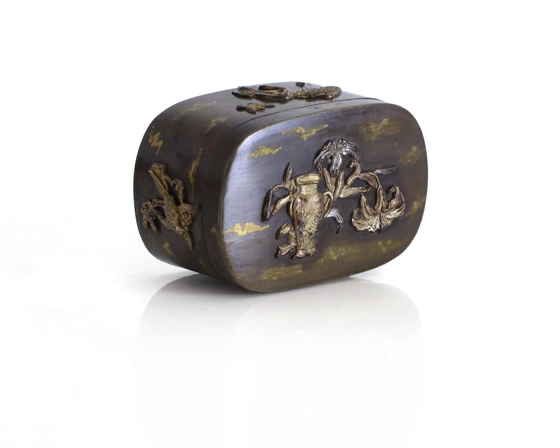 An oval brass lidded box, 20th century,: An oval brass lidded box, 20th century, possibly Japanese, decorated in typical high relief with birds and leafy branches, with patinated clouds to the main ground 6cm wide, 4cm deep, 3cm high