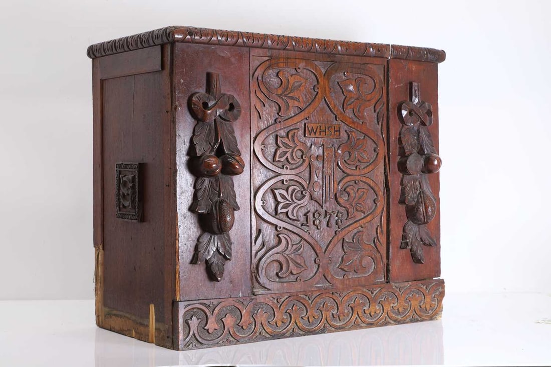 An estate made oak carved box or stick stand, early 20th century,: An estate made oak carved box or stick stand, early 20th century, with a carved front centred with an armorial below 'WHSH', and further scrollwork, flanked with swags of carved fruit, the sides