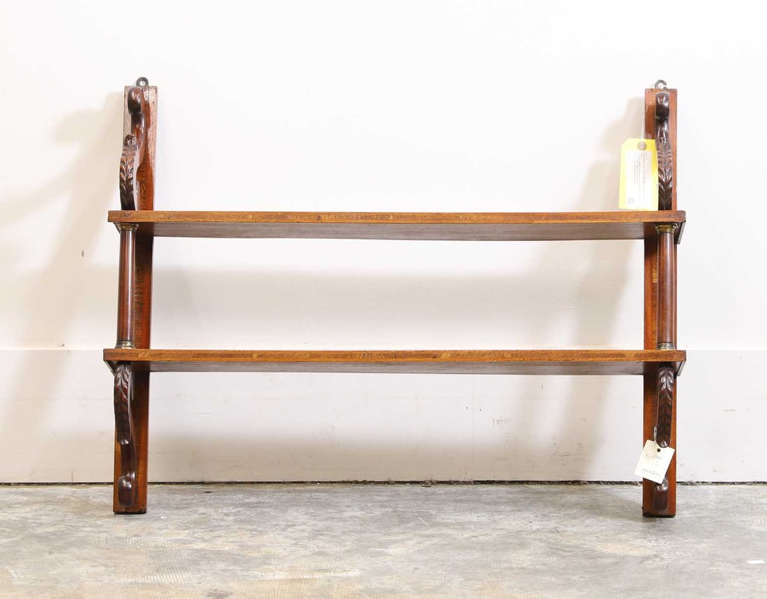 A mahogany wall hanging shelf, 20th century, in the Regency style,: A mahogany wall hanging shelf, 20th century, in the Regency style, with two shaped shelves supported by column uprights with brass collars, and moulded scrolled terminals and leaf ornament, with