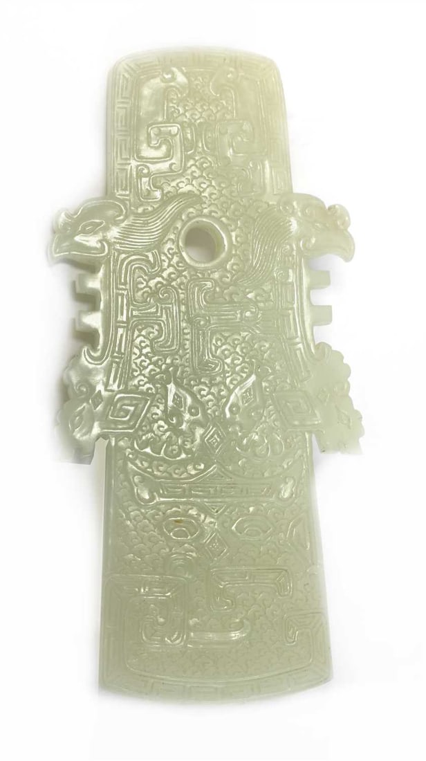 A Chinese jade plaque, possibly Qianlong (1736-1795),: A Chinese jade plaque, possibly Qianlong (1736-1795), in the shape of an archaic ceremonial axe, carved with taotie masks against a diapered ground enclosed by a key fret border, the sides with