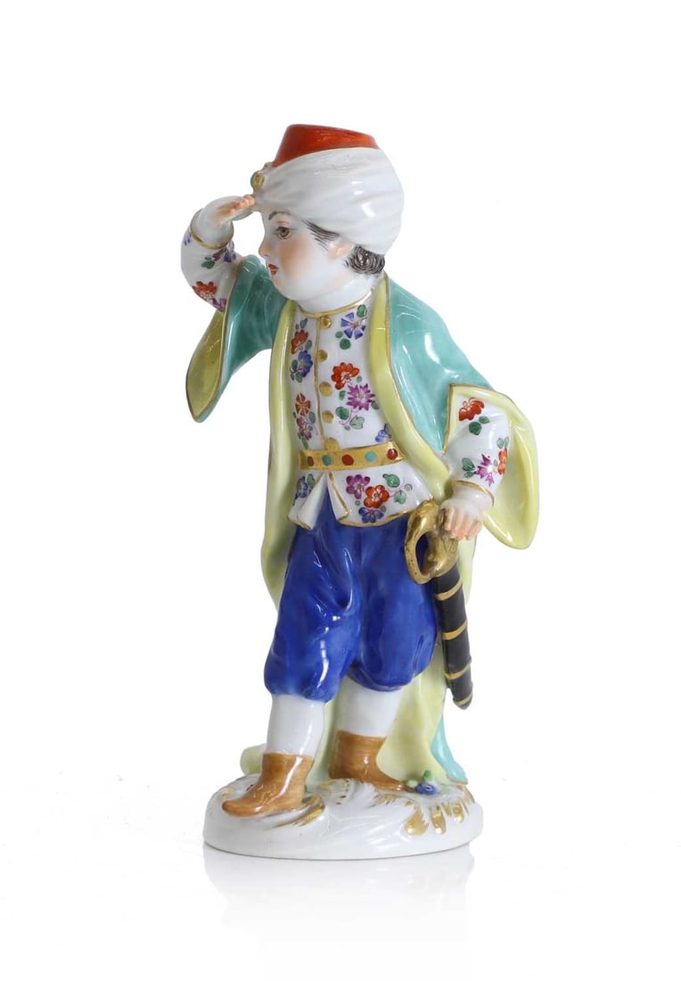 A Meissen figure of a young Turkish boy, late 19th century,: A Meissen figure of a young Turkish boy, late 19th century, modelled as a standing boy in Ottoman dress, wearing a white turban with red cap, and jewelled ornament, a floral painted tunic beneath a p