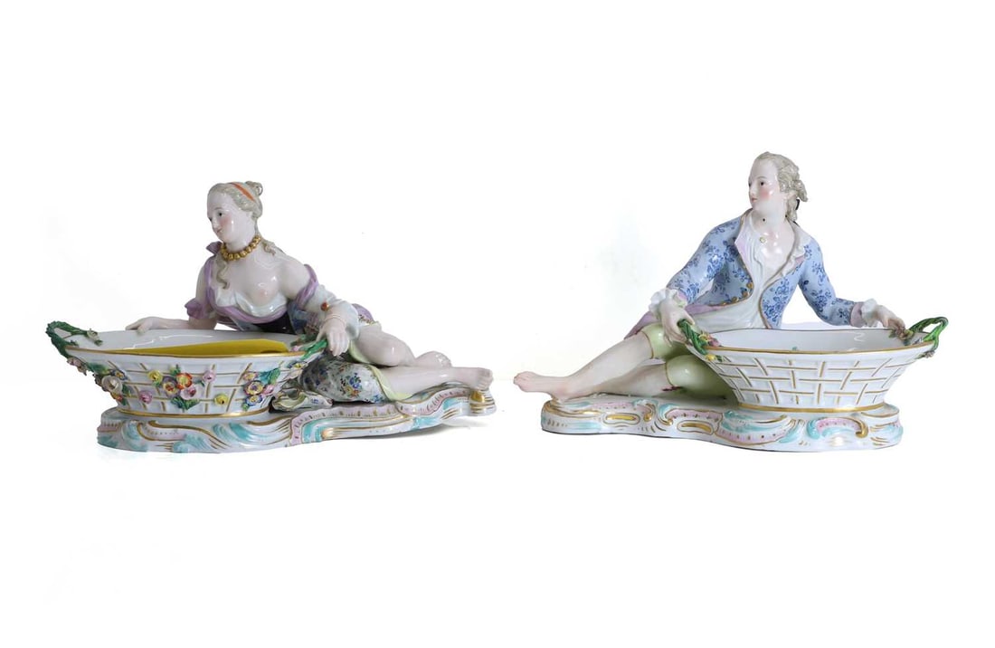 A pair of Meissen sweet dishes, early 19th century,: A pair of Meissen sweet dishes, early 19th century, one modelled as a gallant, the other modelled as a lady, each supporting a floral encrusted oval basket, raised on a scroll moulded base, with